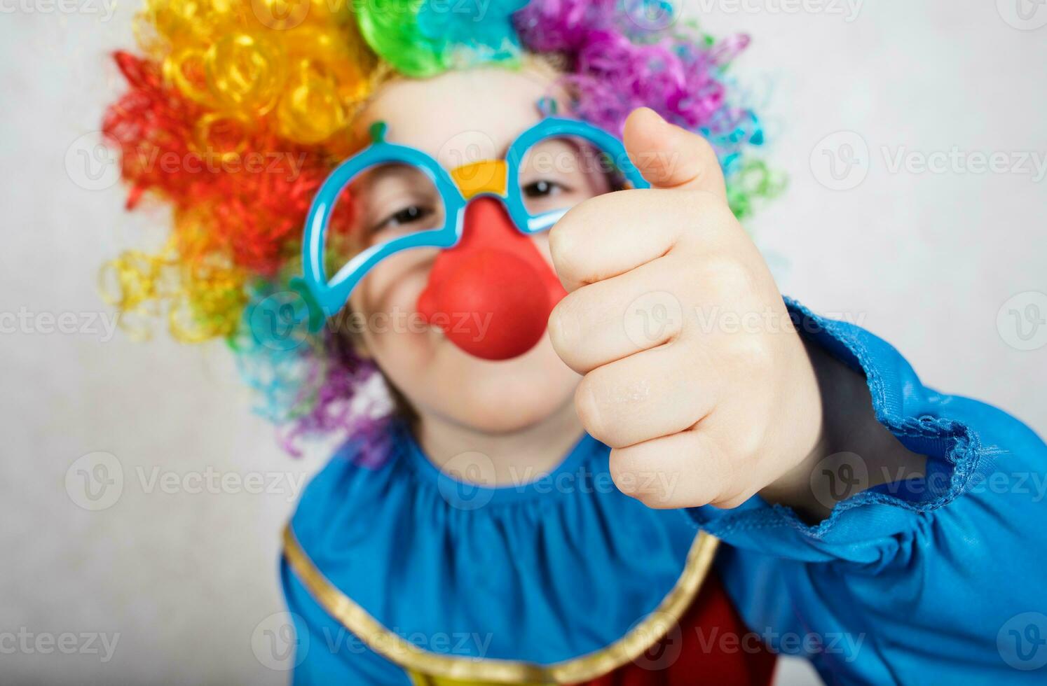 Boy of five years dressed in the costume of a clown and funny eyeglasses with red nose shows his fist photo