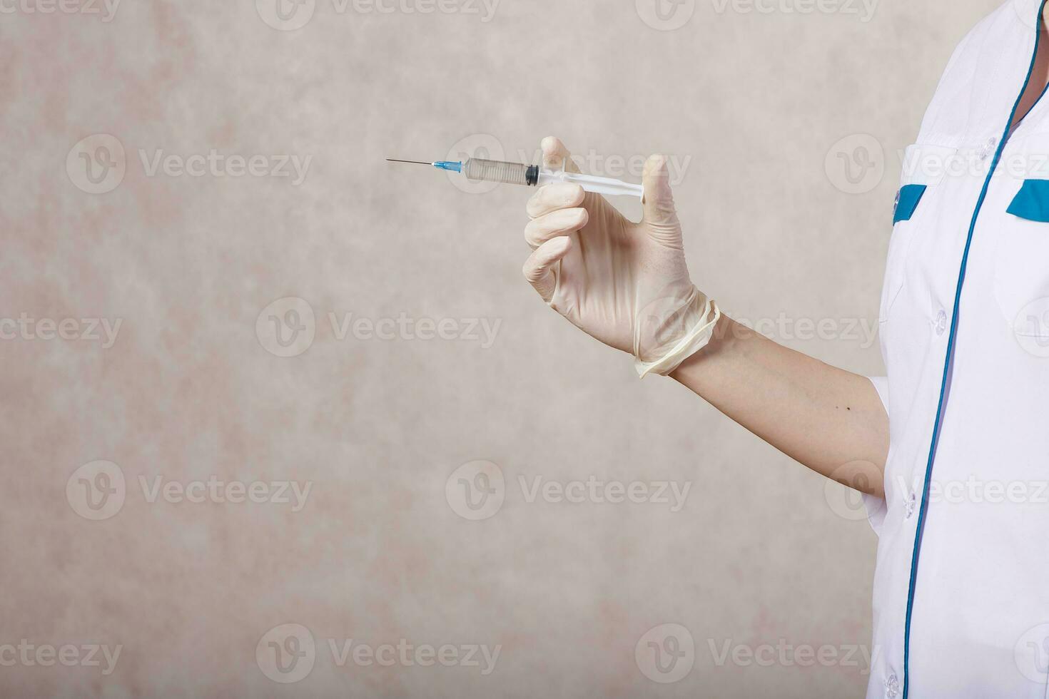 A young cosmetologist dressed in a medical uniform keeps a syringe photo