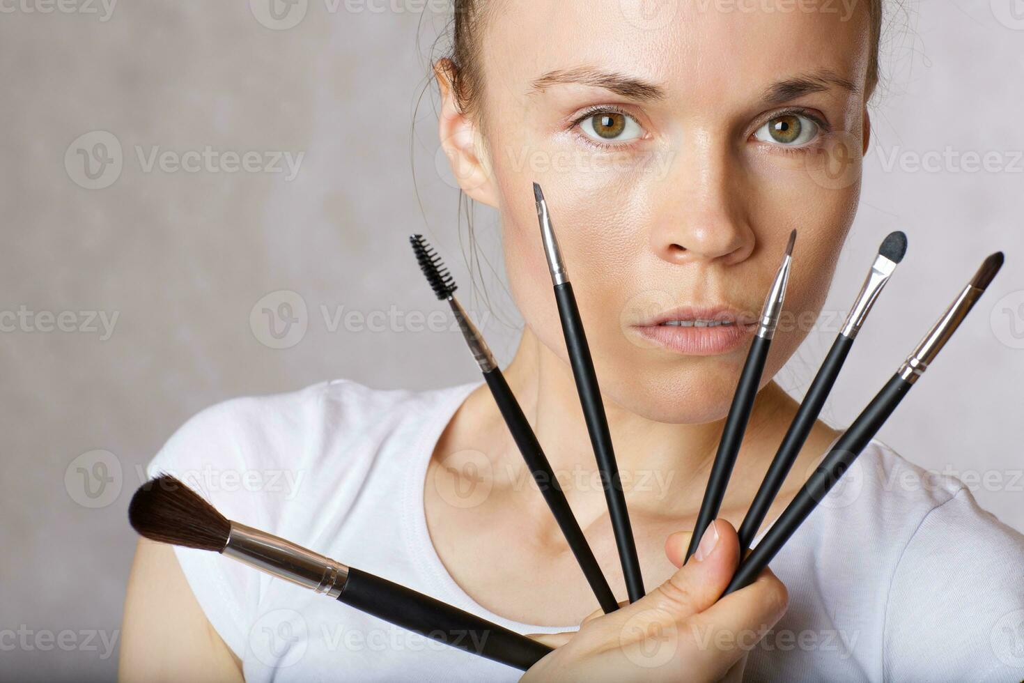 Young lady keeps make up brushes kit close to her face. Closeup photo