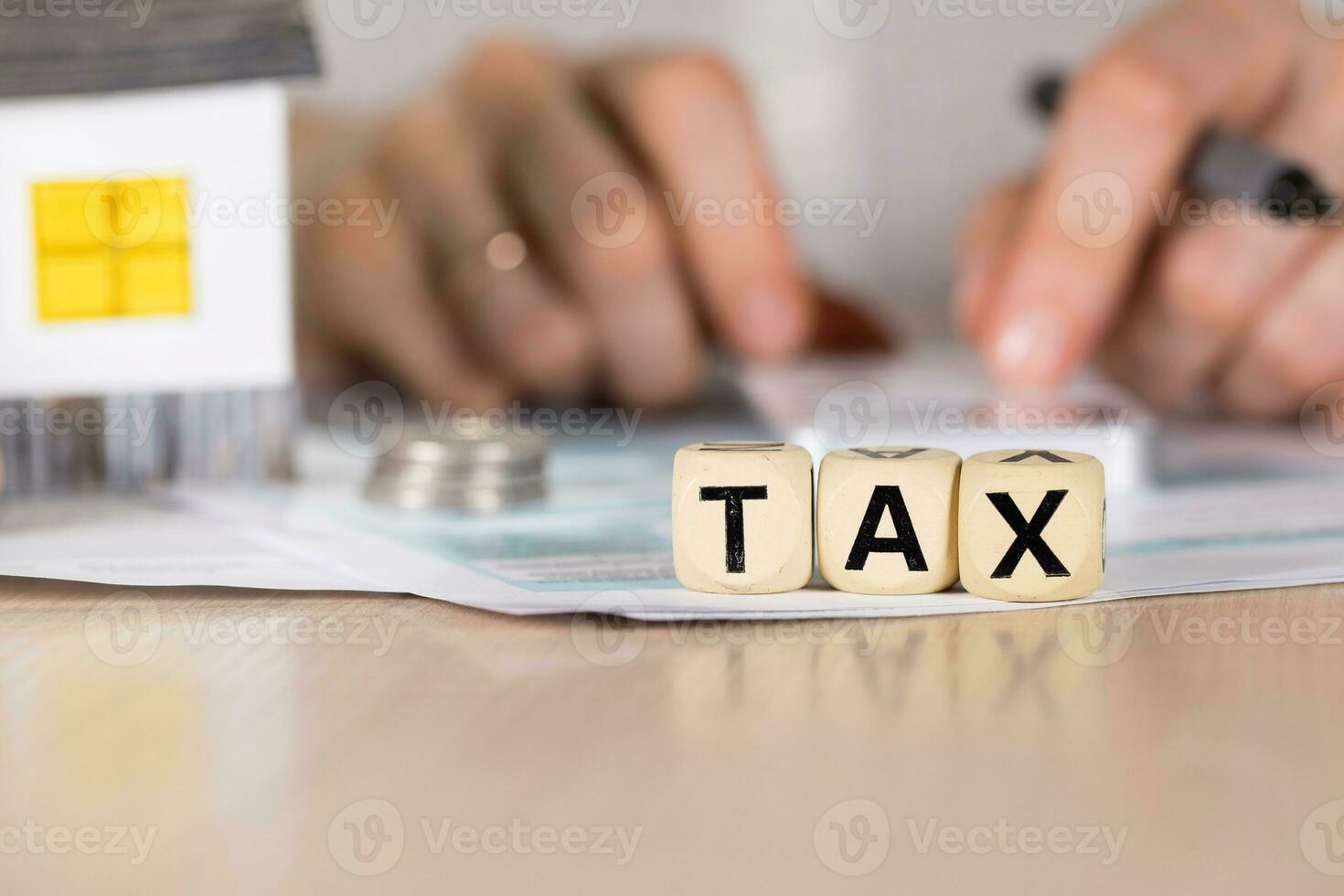 Word TAX composed of wooden letters. Female hand with a pen in the background. photo