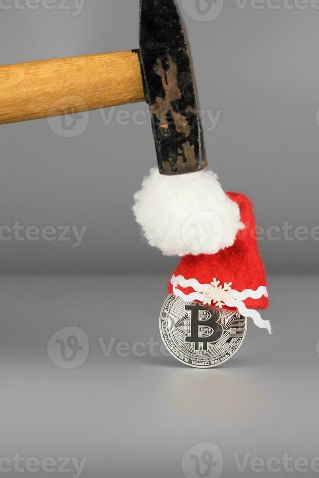 Bitcoin in a Santa Claus hat and a hammer on a gray surface. photo
