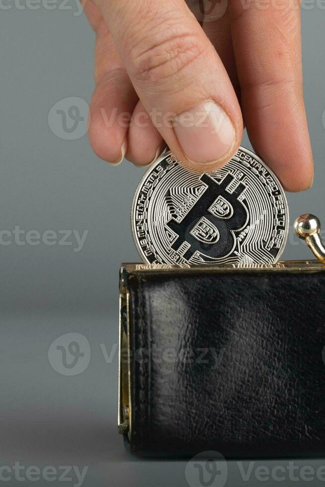 Person puts bitcoin in a black wallet. photo