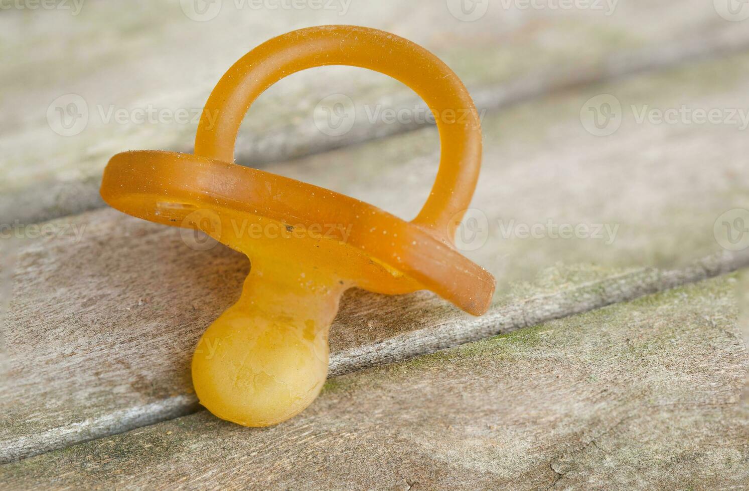 A dirty rubber pacifier on a wooden surface. Closeup photo