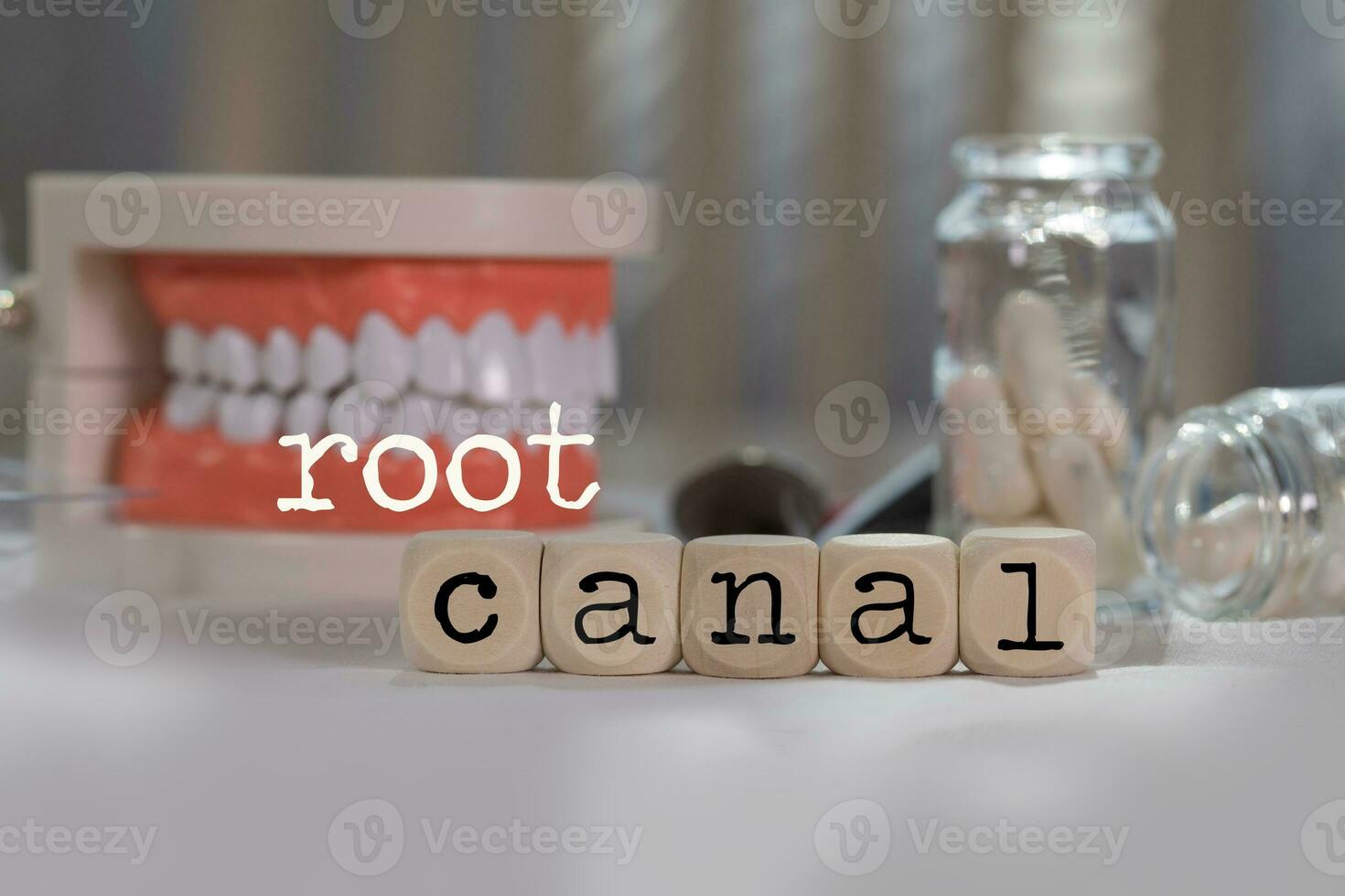 Words ROOT CANAL composed of wooden dices. Pills, documents, pen, human jaw model in the background. photo