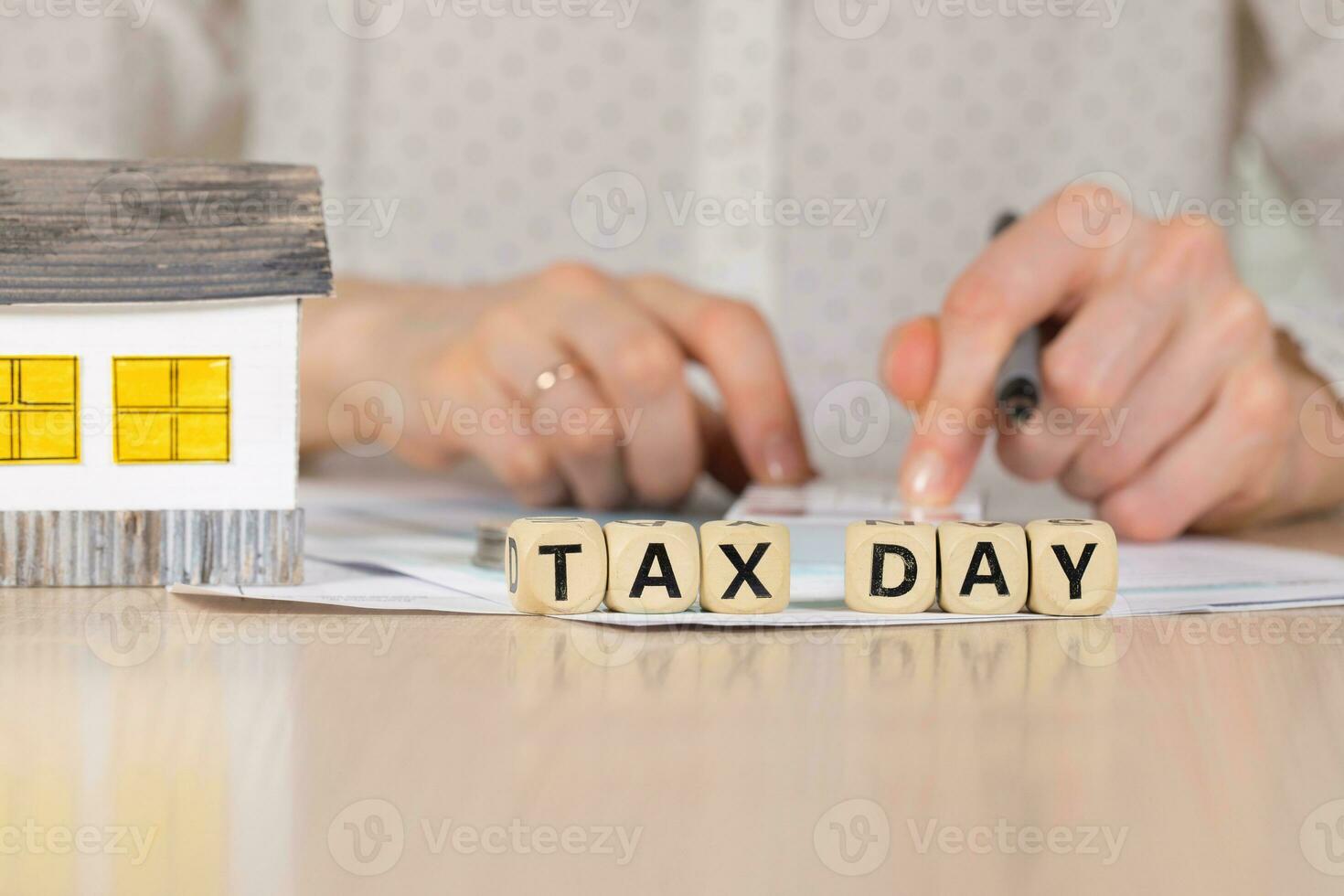 Word TAX DAY composed of wooden letters. Female hand with a pen in the background. photo