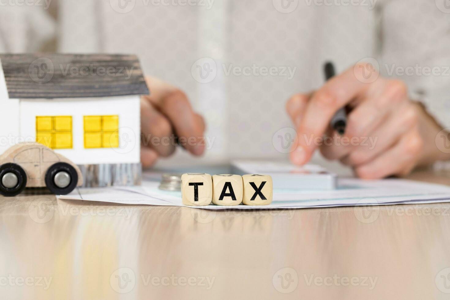 Word TAX composed of wooden letters. Female hand with a pen in the background. photo