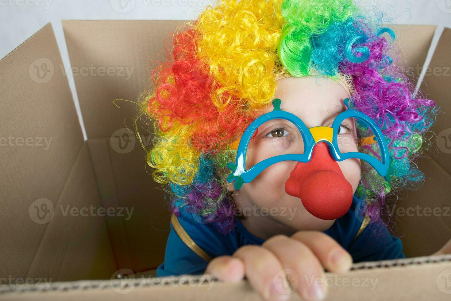 Boy of five years dressed in the costume of a clown stays in a carton paper box. photo