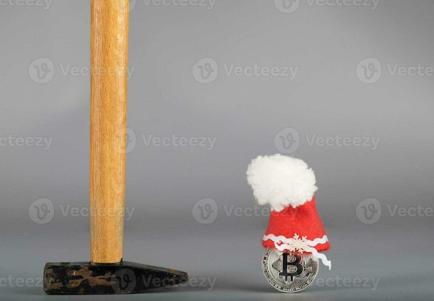 Bitcoin in a Santa Claus hat and a hammer on a gray surface. photo