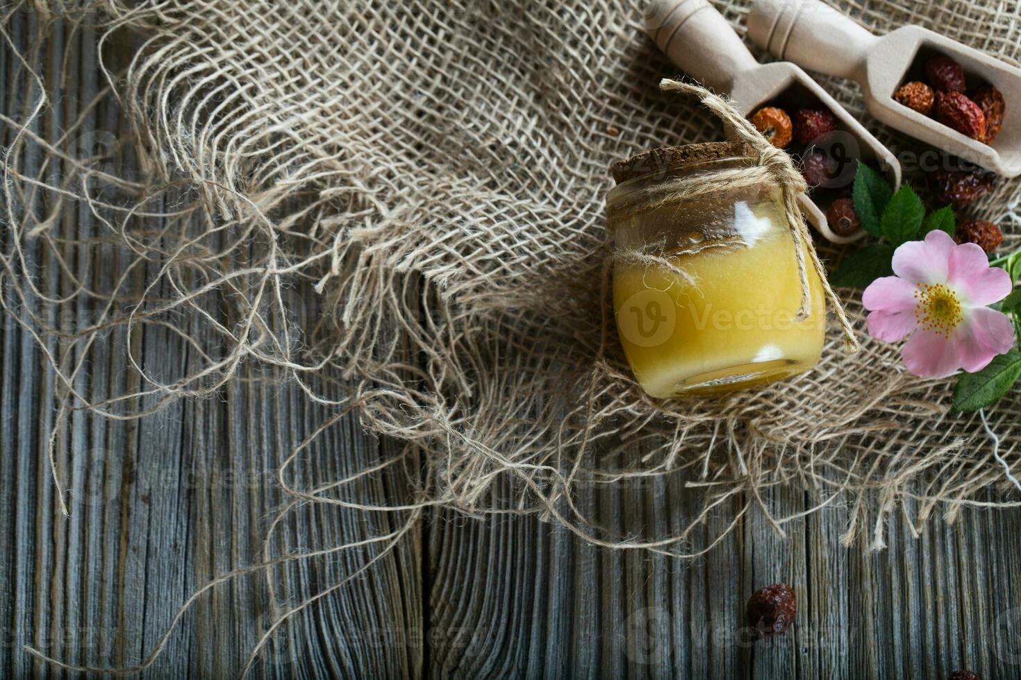 Wild rose hip honey in a glass bottle on a wooden surface. photo