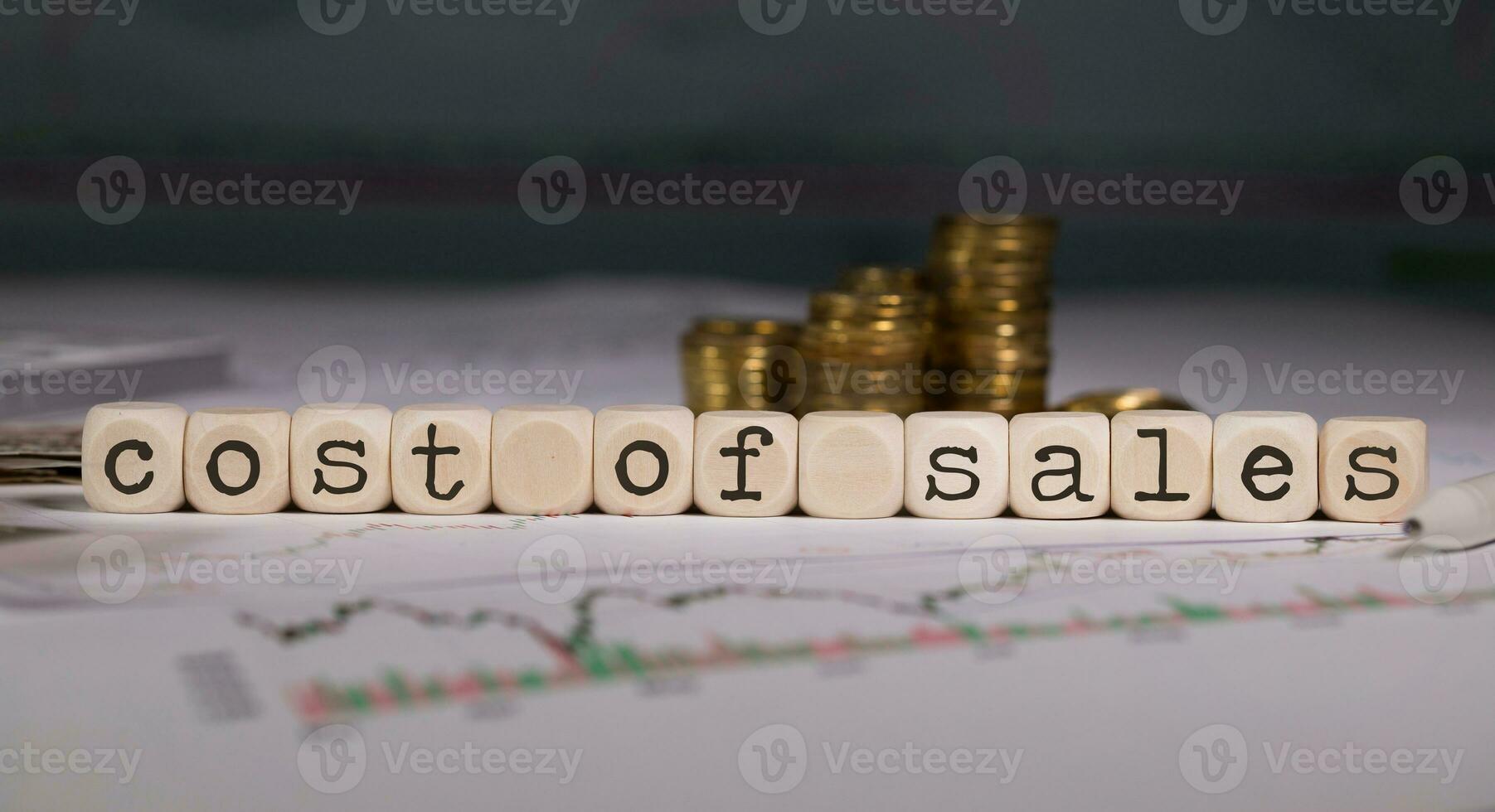 Term COST of SALES composed of wooden letter. Stacks of coins in the background. photo