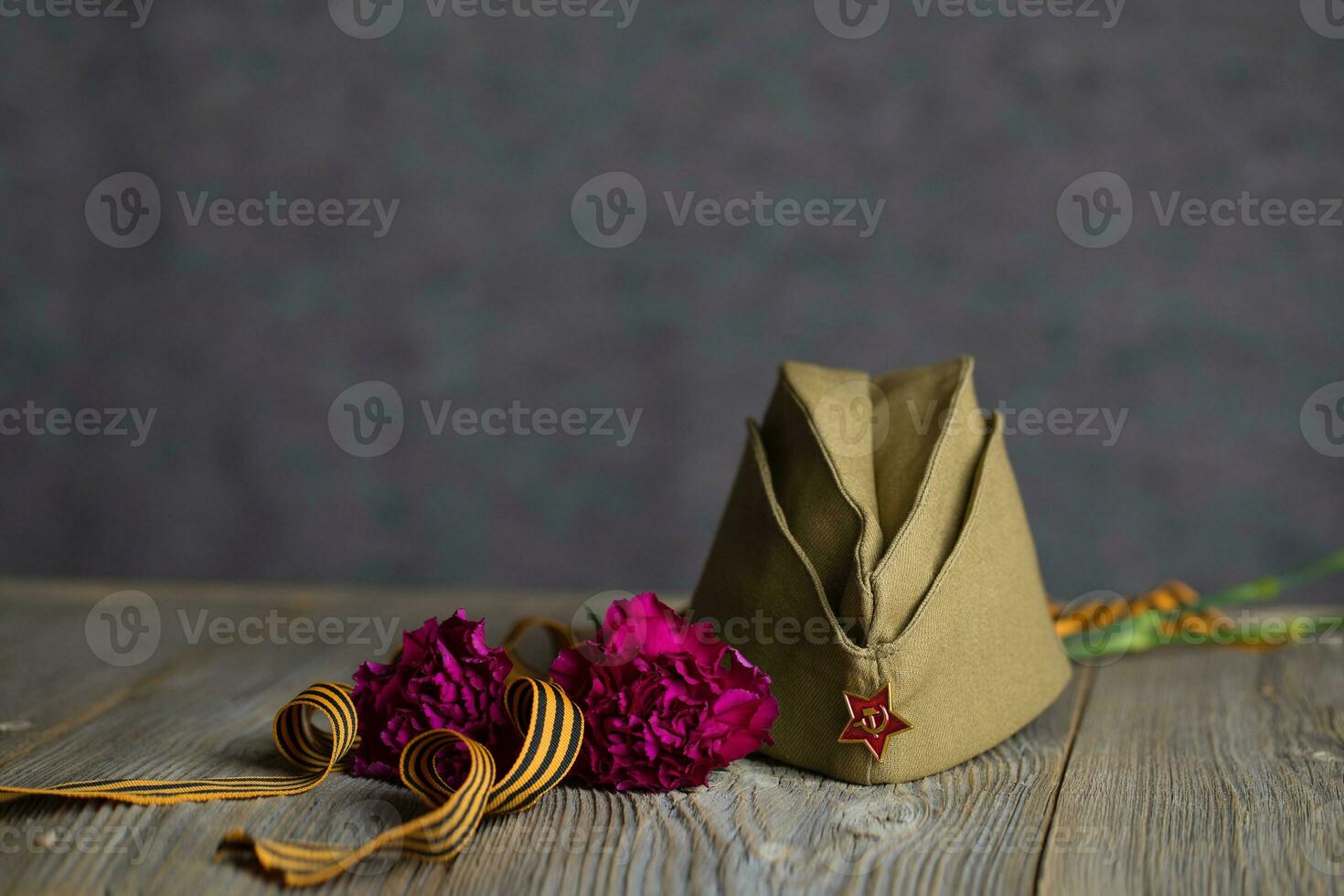 Military cap, carnations, Saint George ribbon on a wooden surface. photo