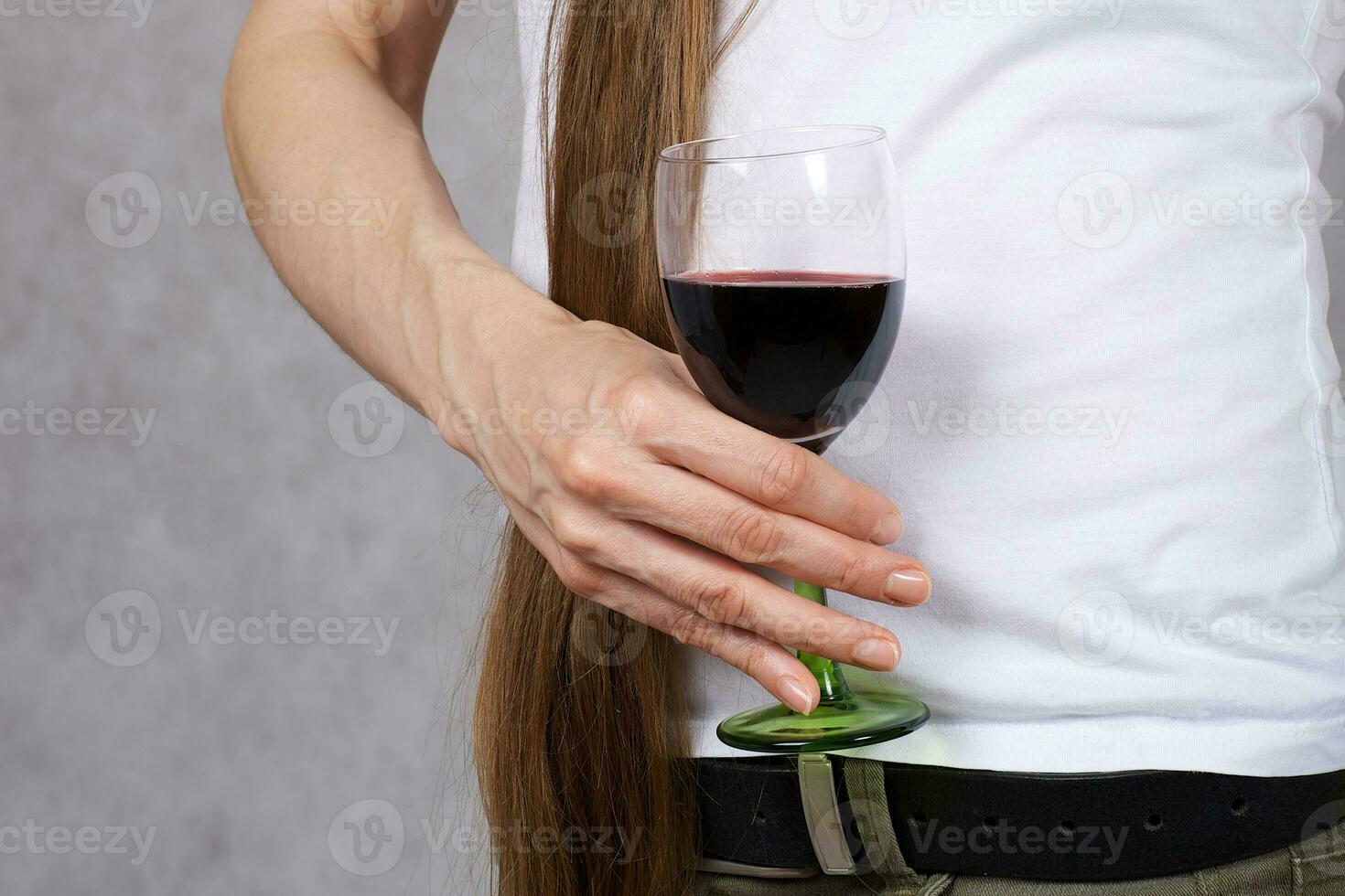 joven dama vestido en pantalones mantiene un vaso de rojo vino. de cerca foto