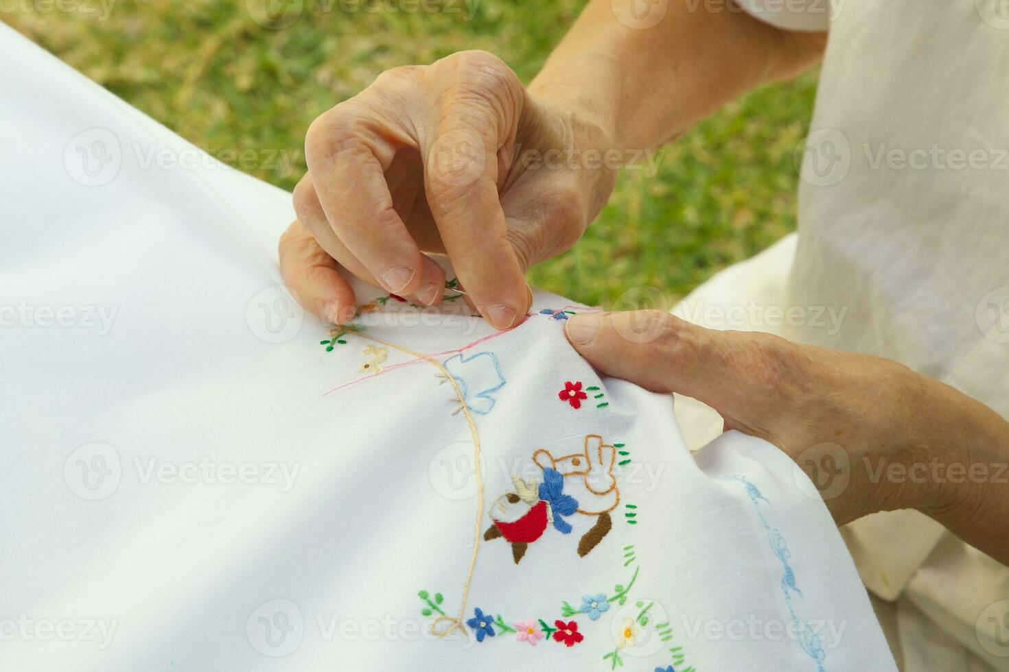 An old woman is embroidering on the white blanket photo