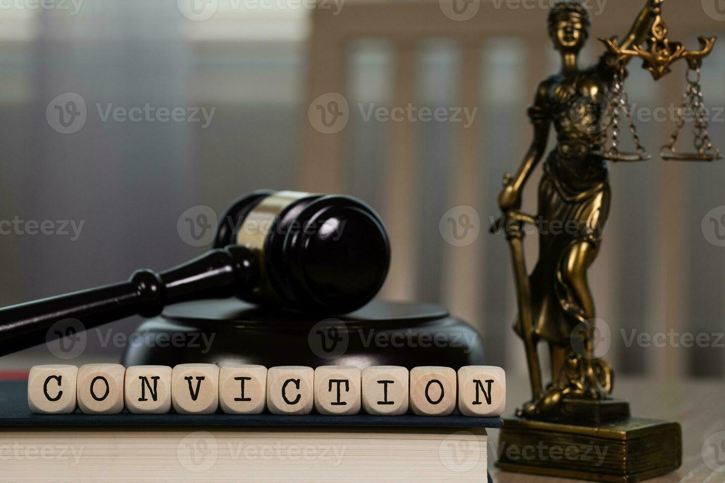 Word CONVICTION composed of wooden dices. Wooden gavel and statue of Themis in the background. photo