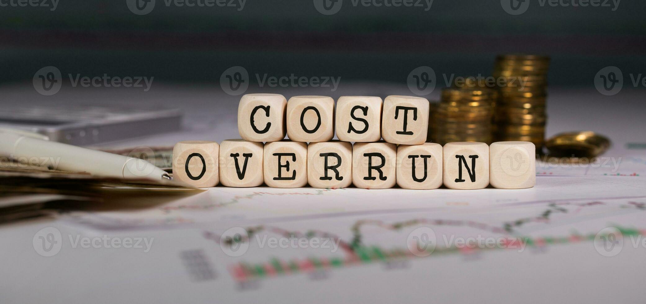 Words COST OVERRUN  composed of wooden letter. Stacks of coins in the background. photo