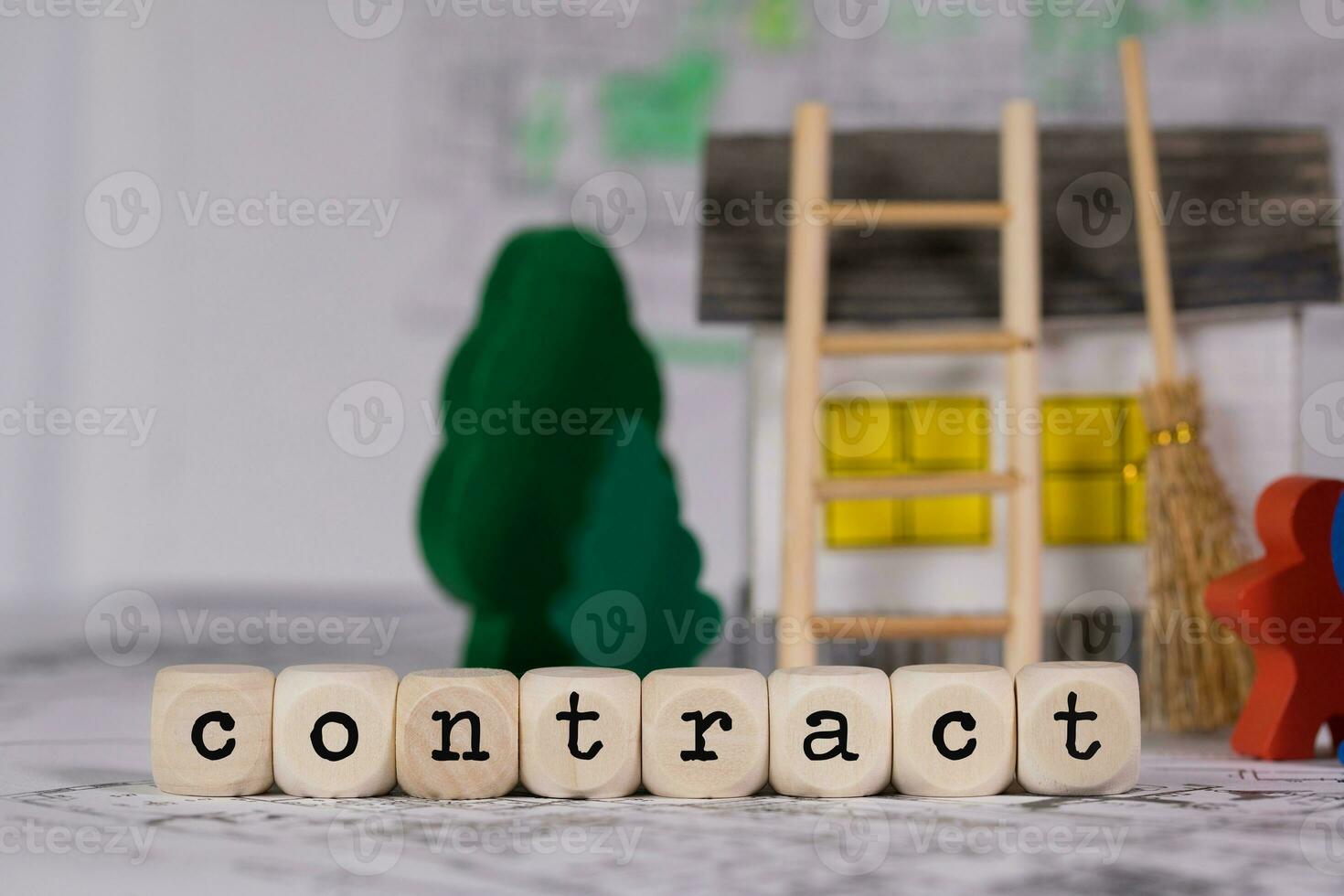 Word  CONTRACT composed of wooden letter. Small paper house, wooden trees in the background. photo