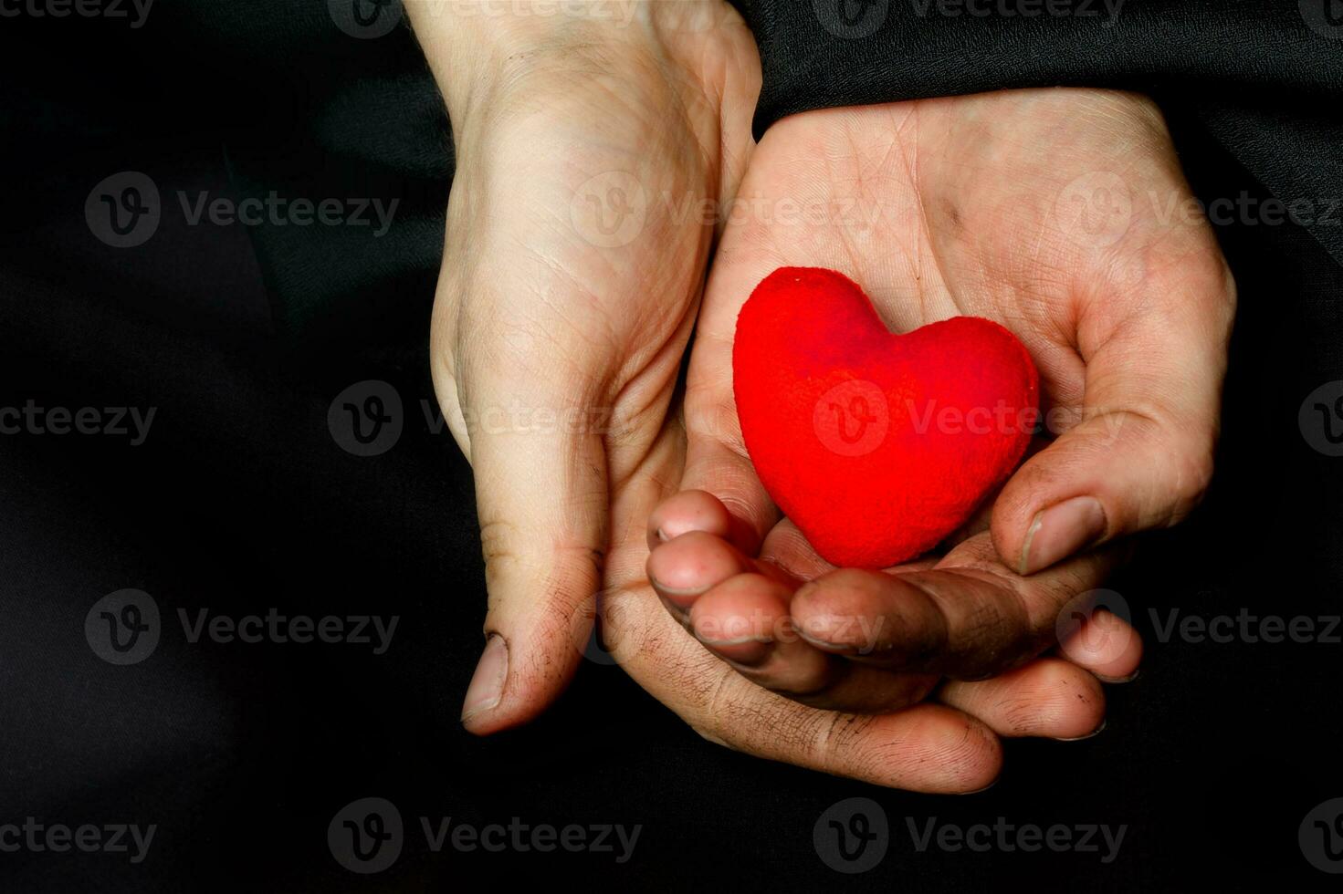 Palm of a peasant woman with plush red heart on a black fabric. photo