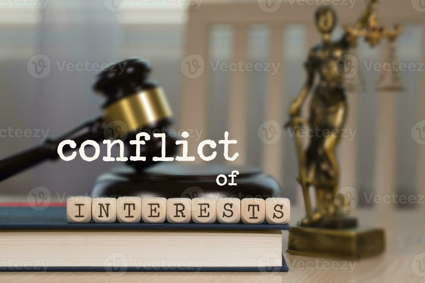 Words CONFLICT OF INTERESTS composed of wooden dices. Wooden gavel and statue of Themis in the background. photo