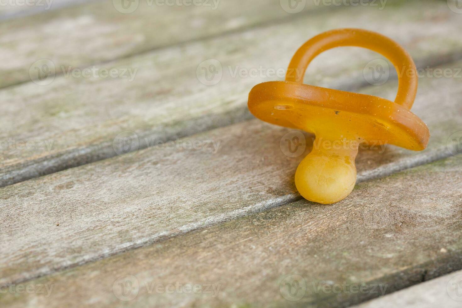 A dirty rubber pacifier on a wooden surface. Closeup photo