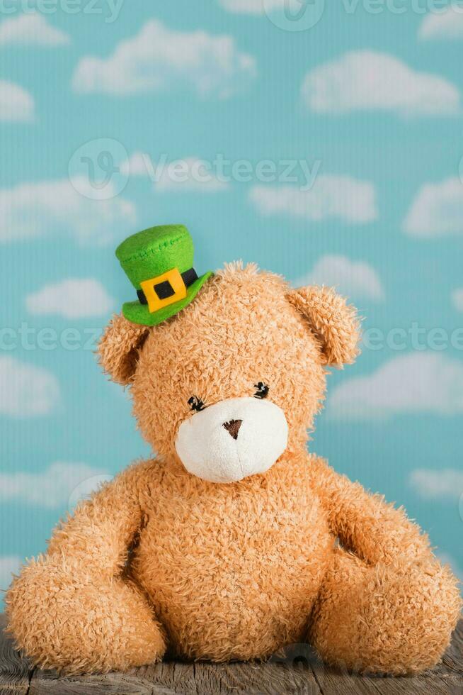 Brown plush teddy bear in a leprechaun hat on a wooden surface. photo