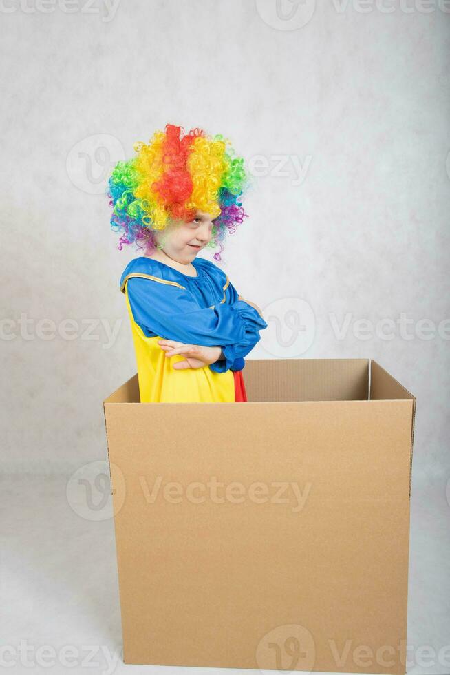 Boy of five years dressed in the costume of a clown stays in a carton paper box. photo
