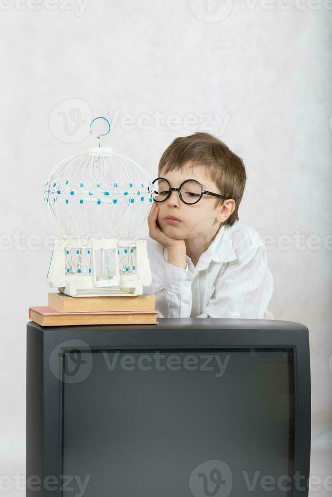 Boy of seven years old looks at white cage which is laced on old TV. photo