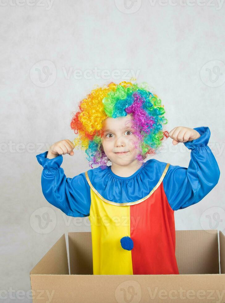 Boy of five years dressed in the costume of a clown stays in a carton paper box. photo