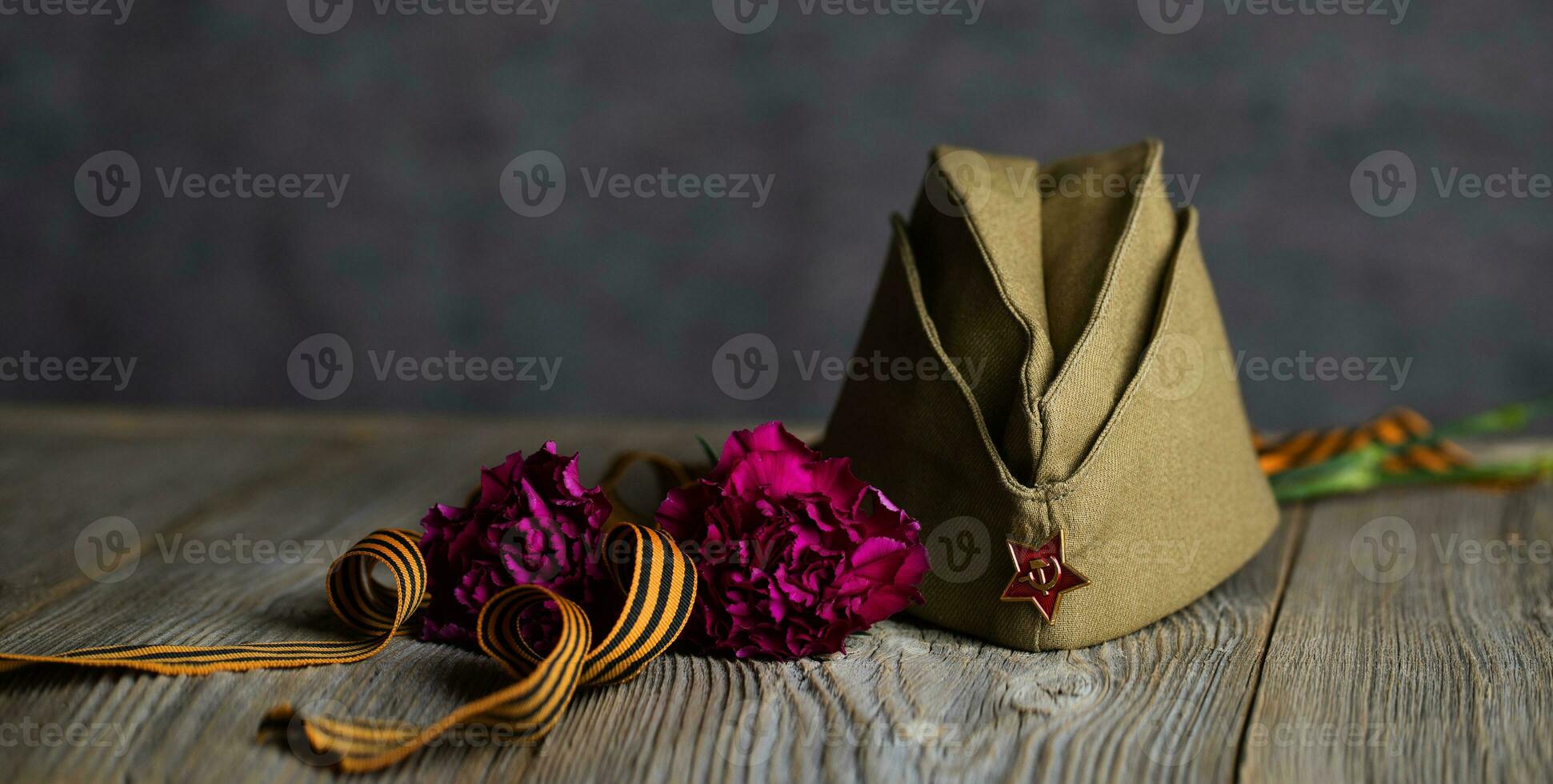 Military cap, carnations, Saint George ribbon on a wooden surface. photo