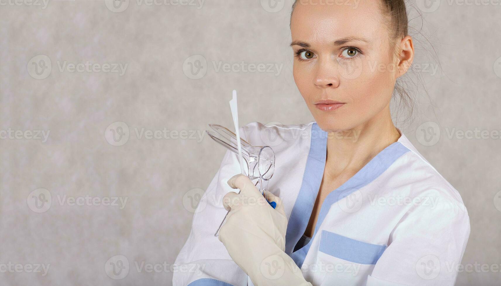 Young female gynecologist with vaginal speculum on a gray background. photo