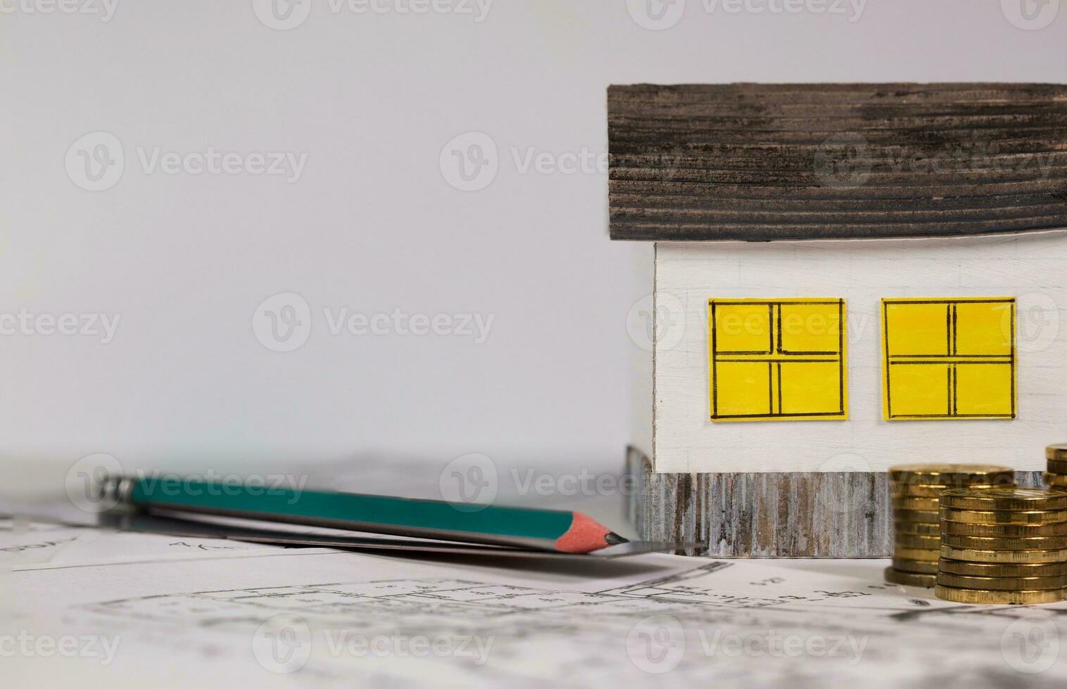 Paper house, stacks of coins, coal pencil and metal ruler on a technical drawing. photo