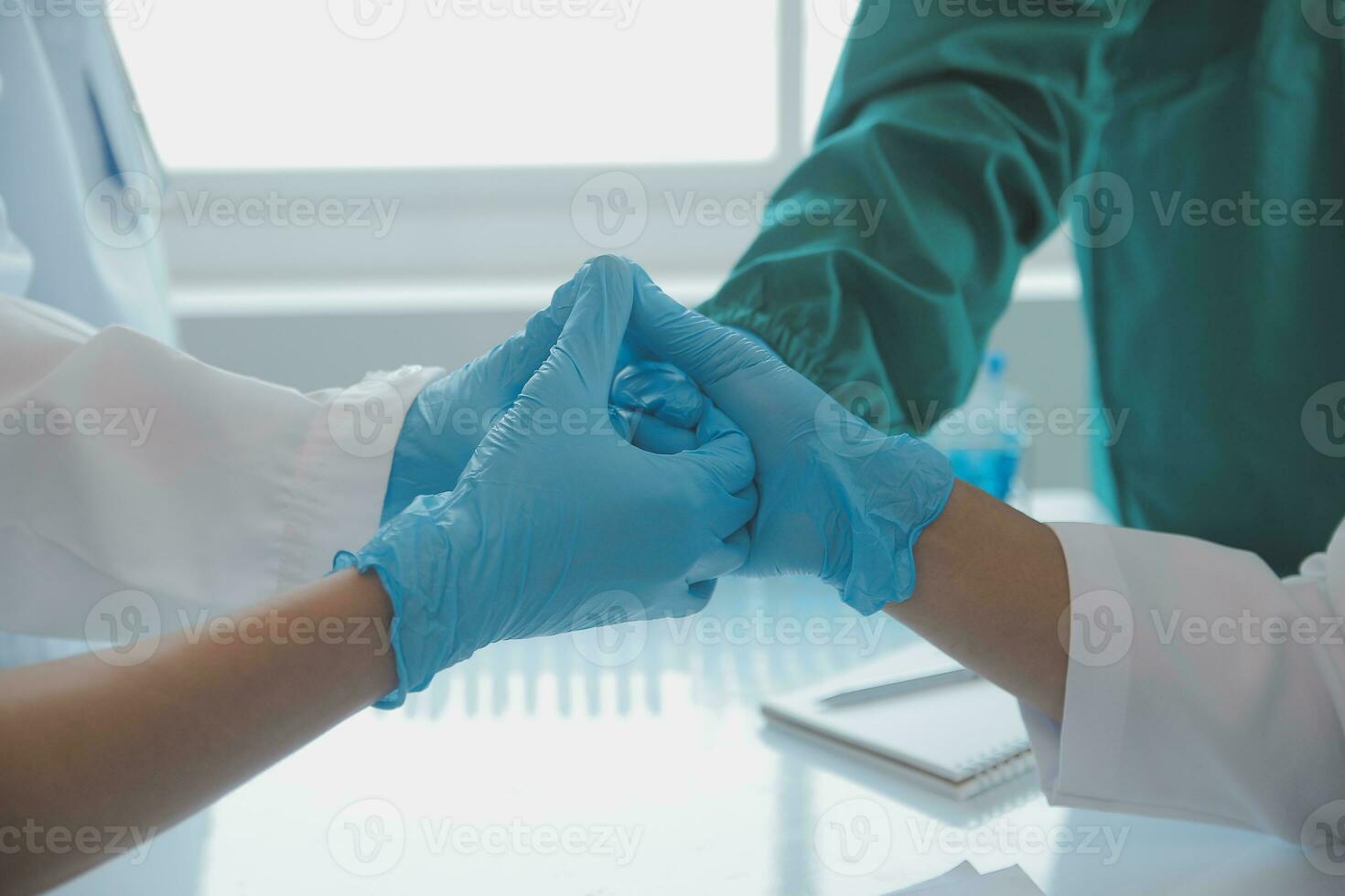Multiracial medical team having a meeting with doctors in white lab coats and surgical scrubs seated at a table discussing a patients records photo