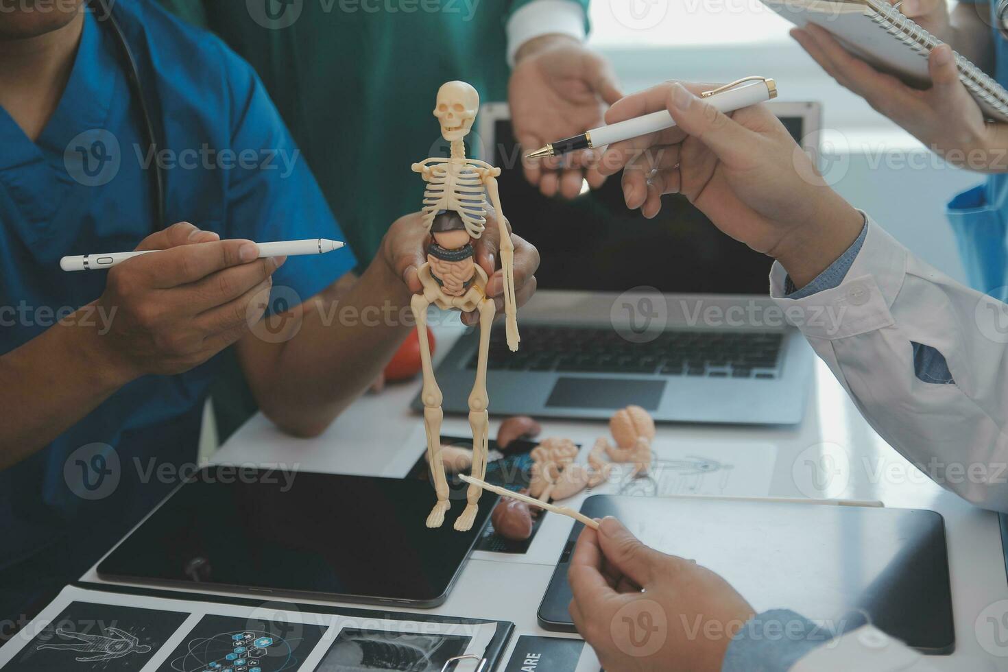 Multiracial medical team having a meeting with doctors in white lab coats and surgical scrubs seated at a table discussing a patients records photo