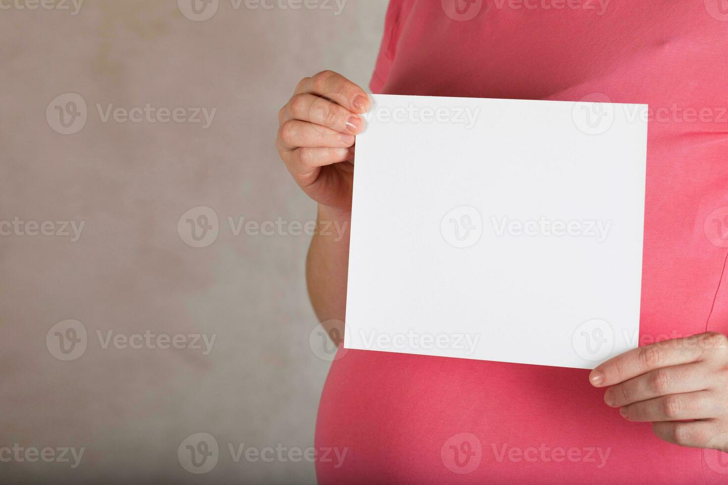 Young pregnant between 30 and 35 years old woman keeps a  blank white sheet of paper. photo