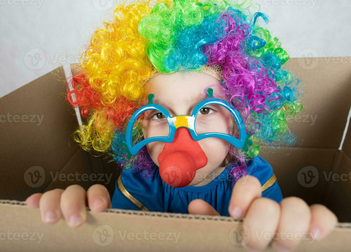 Boy of five years dressed in the costume of a clown stays in a carton paper box. photo