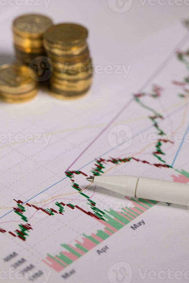 Pen on a colourful diagram. Coins in the background. photo