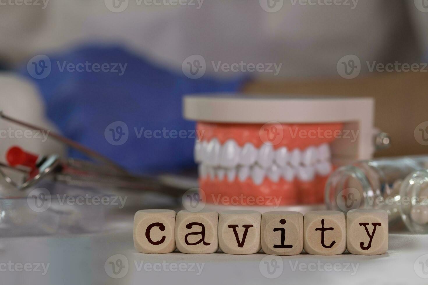 Word CAVITY composed of wooden dices. Pills, documents, pen, human jaw model in the background. photo