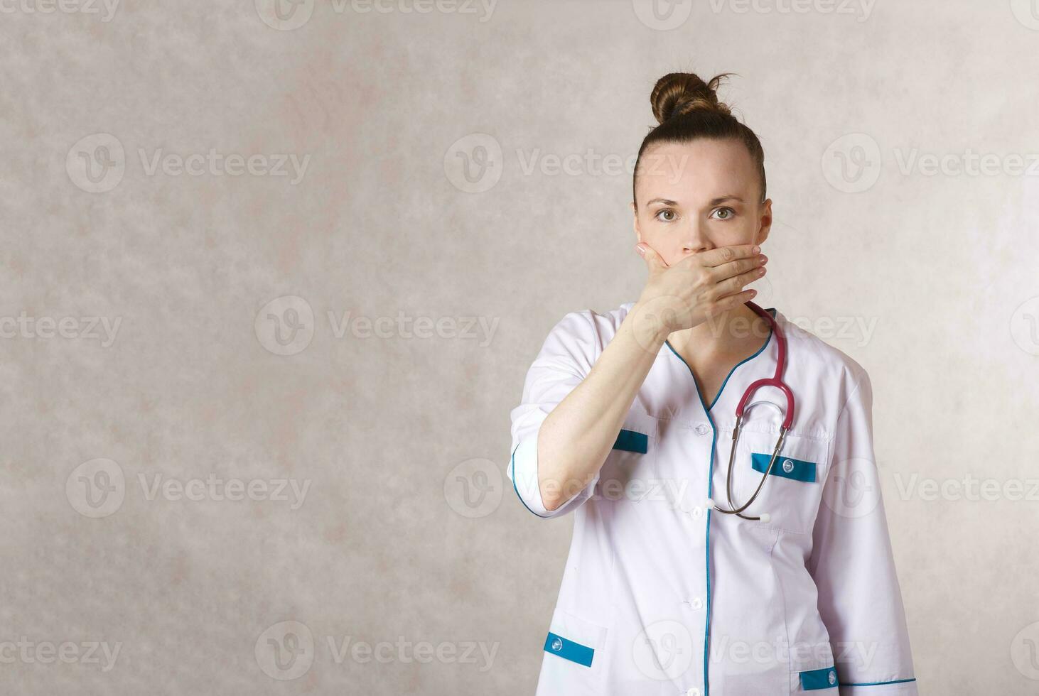 Young female doctor dressed in a white medical uniform with a covered mouth photo