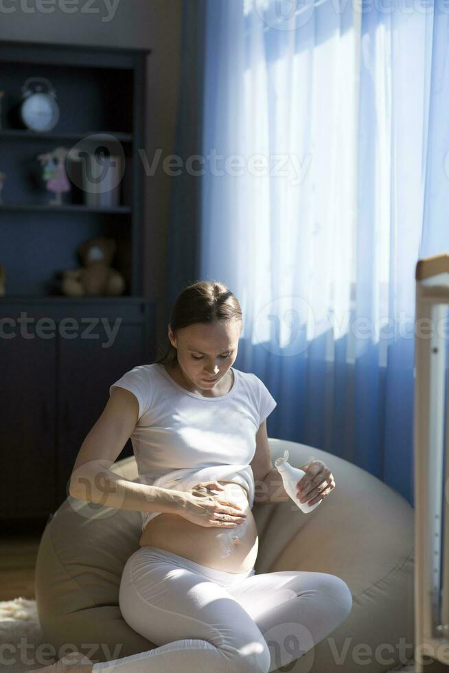 Young pregnant lady is putting cream on her belly photo