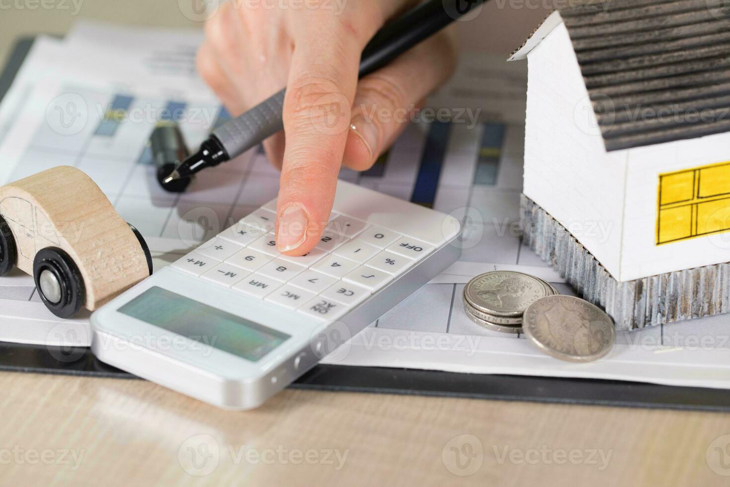 Young woman makes some calculations. Small paper house, coins, car in the background. photo