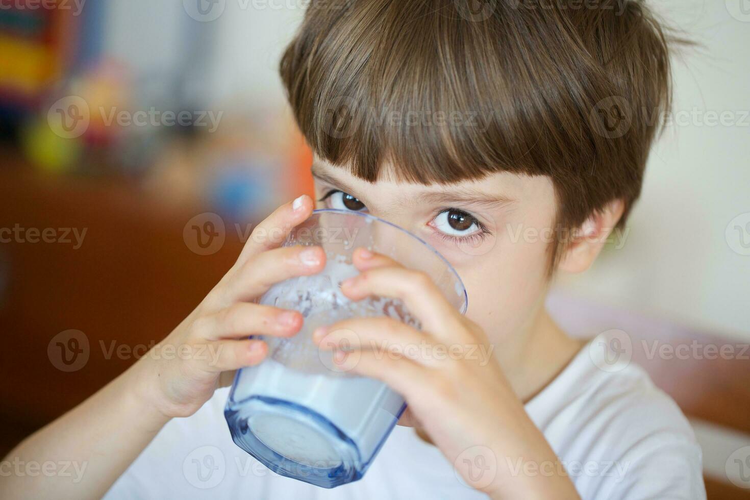 Boy of six years is taking a glass of warm milk with oat biscuits. photo