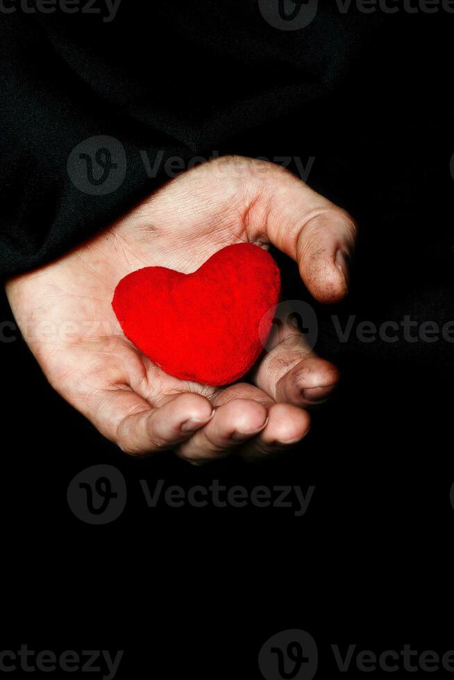 Palm of a peasant woman with plush red heart on a black fabric. photo