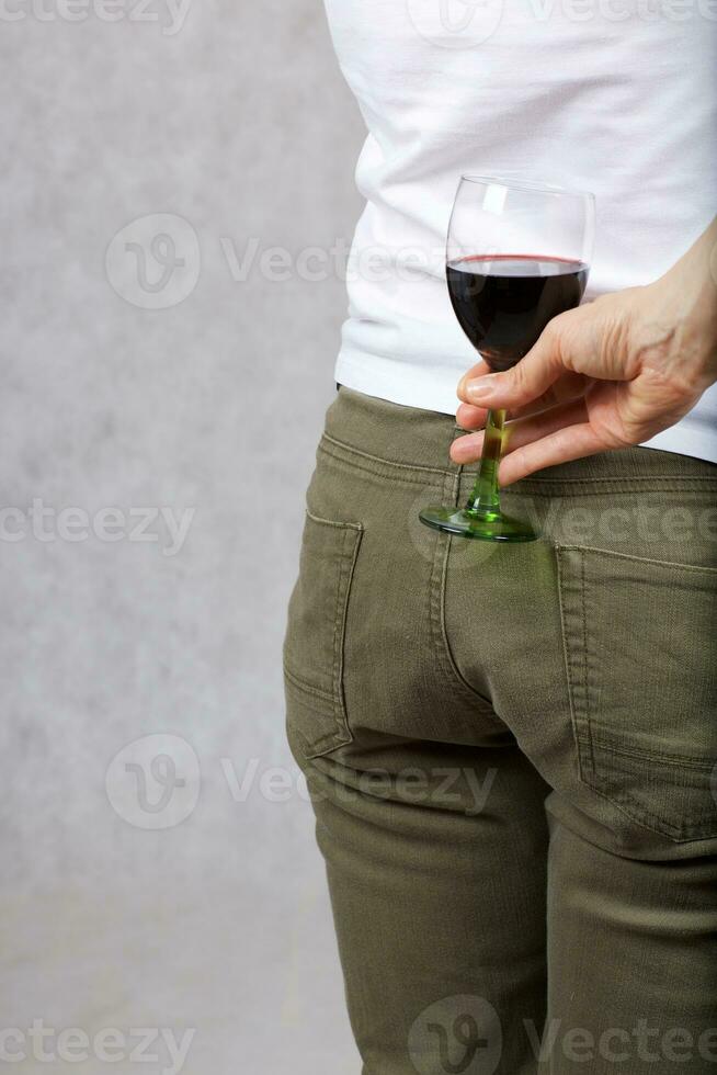 Young lady dressed in jeans keeps a glass of red wine. Closeup photo