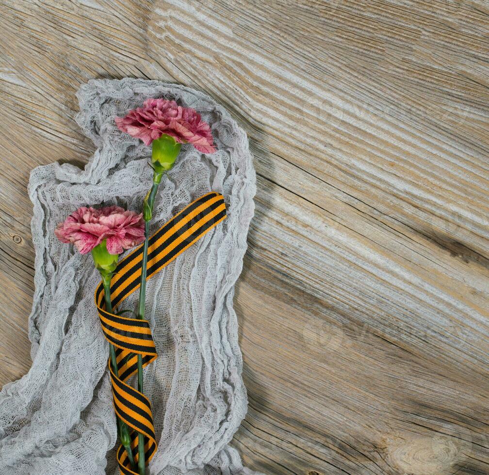 Two pink carnations, Saint George ribbon on a wooden surface. photo