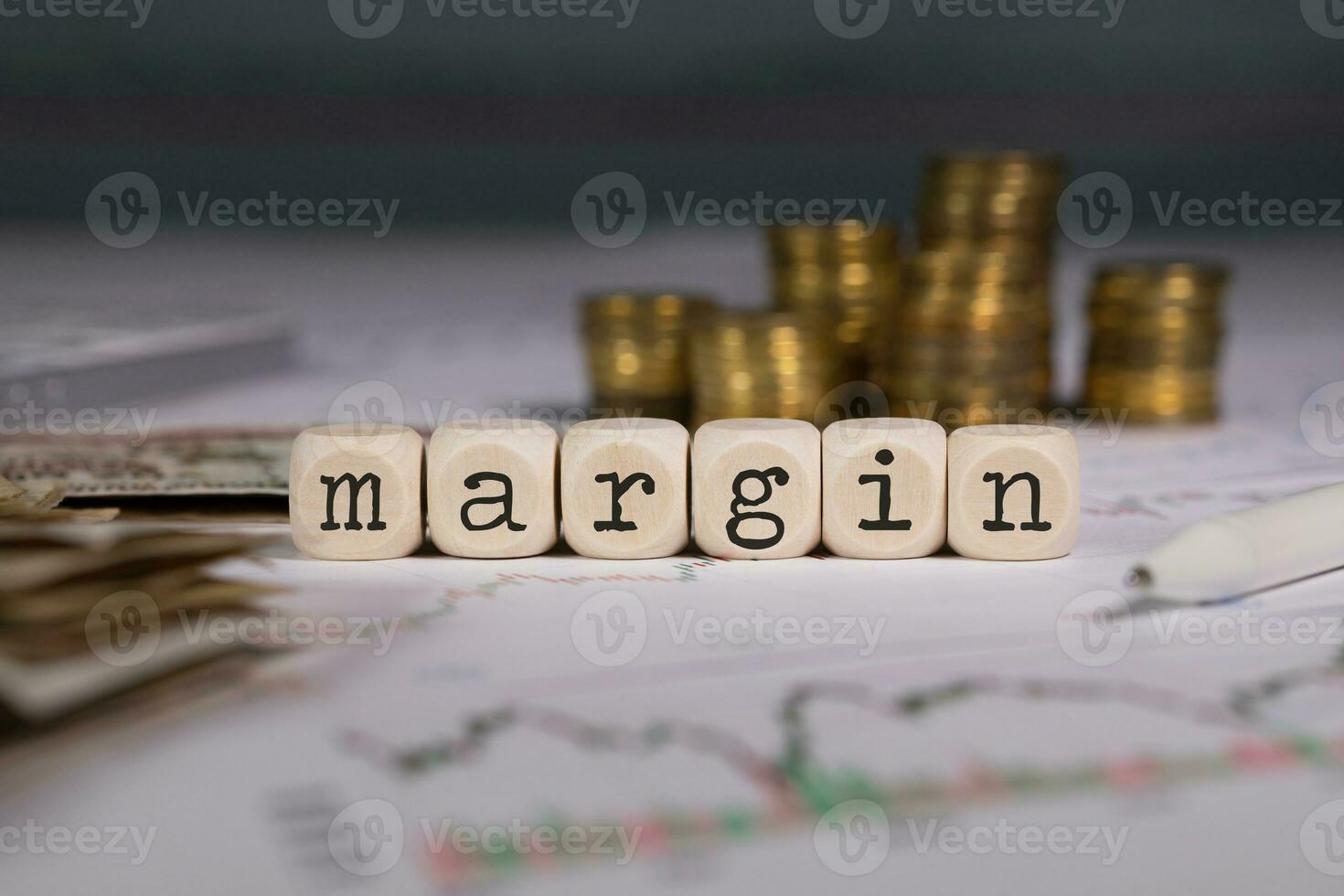 Word MARGIN composed of wooden letter. Stacks of coins in the background. photo