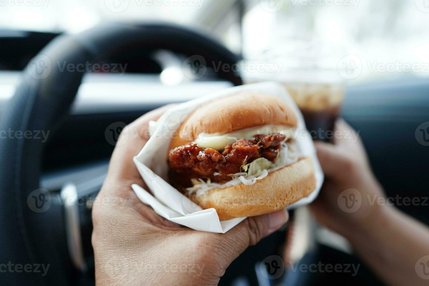 asiático mujer conductor sostener y comer hamburguesa en auto, peligroso y riesgo un accidente. foto