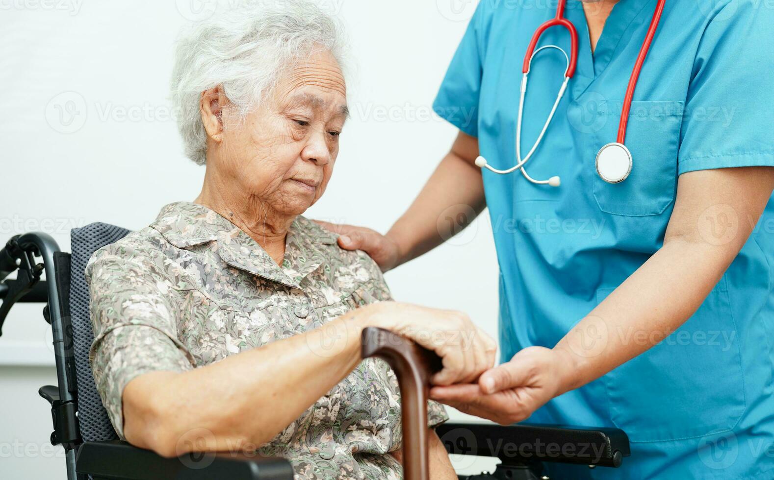 Doctor help Asian elderly disability woman patient holding walking stick in wrinkled hand at hospital. photo