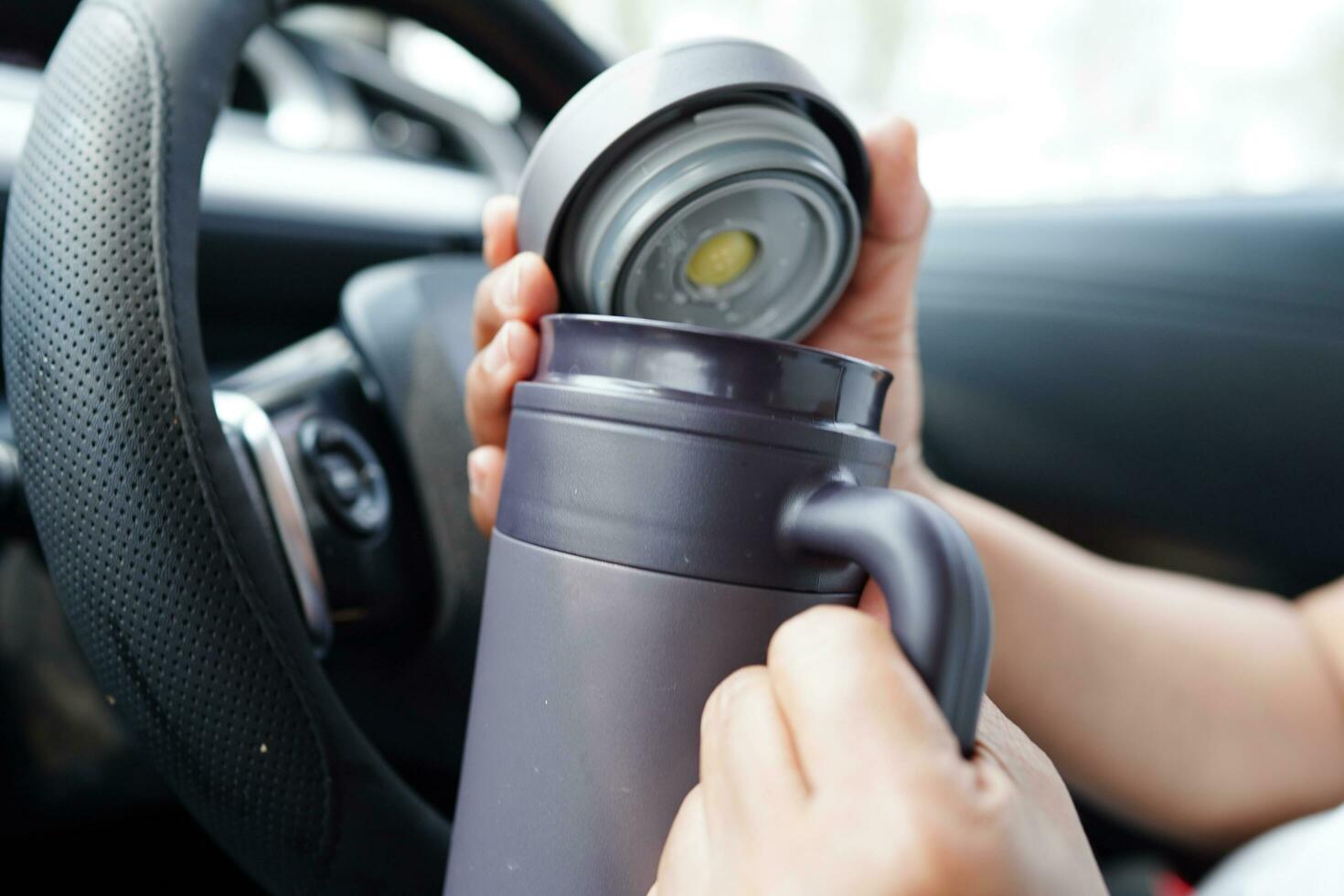 Asian woman driver hold thermo mug with hot coffee in car, dangerous and risk an accident. photo