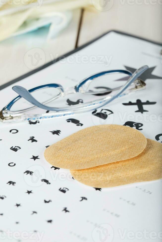 Eyeglasses for children on a eye chart close to eye pads. photo