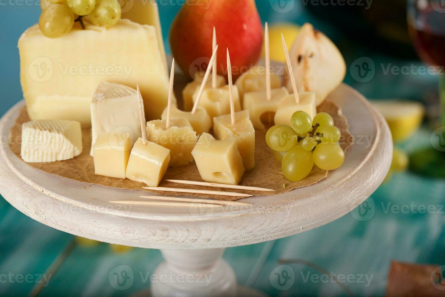 Cheese slices, pear, and grapes on a wooden stand. photo
