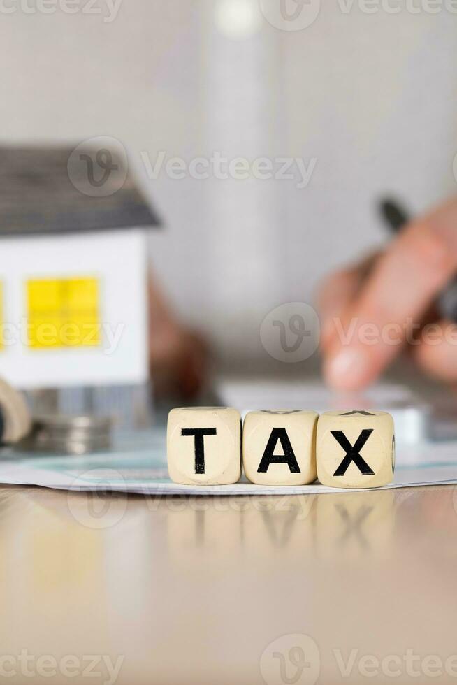 Word TAX composed of wooden letters. Female hand with a pen in the background. photo